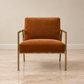 Load image into Gallery viewer, A modern accent chair with a warm rust-orange velvet upholstery and a slim brass metal frame, set against a neutral beige wall and marble floor.
