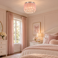 Load image into Gallery viewer, A pink crystal chandelier with a silver-toned metal frame and a pink textured drum shade hangs in a beautifully decorated pink bedroom with white furniture, blush curtains, and a bed with pink and white bedding.
