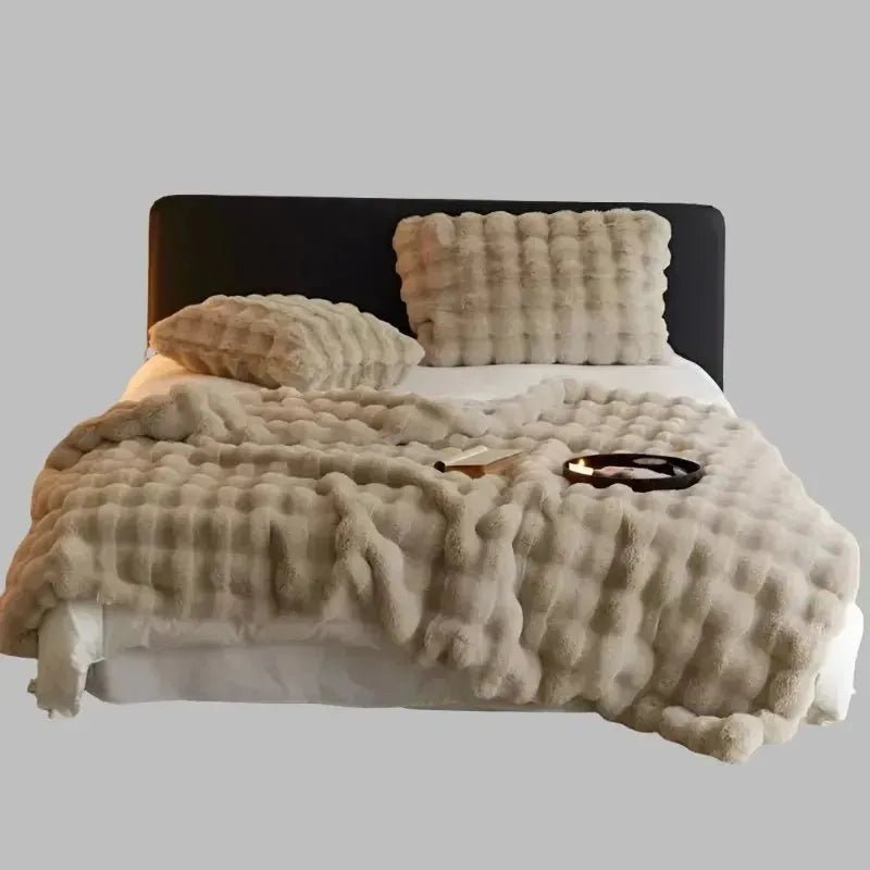 A neatly made bed with a black headboard, featuring a fluffy beige comforter and pillows, highlighted by a House of Effy TUSCAN THROW for extra winter warmth, with an open book and glasses placed on top.