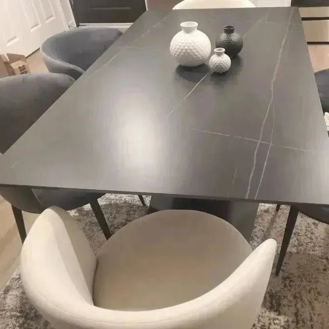 A rectangular BLACK MARBLE TABLE by House of Effy with a white and black striped pattern on the surface, surrounded by grey and white chairs, holds a variety of white and black ceramic vases in the center.