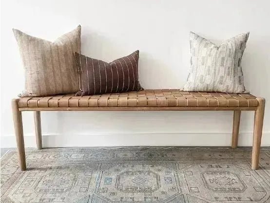 A sleek, contemporary WOODEN CONTEMPORARY BENCH with three patterned pillows sits against a white wall on a patterned rug, showcasing its premium quality wood. This product is from House of Effy.