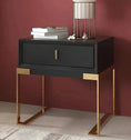 Load image into Gallery viewer, A House of Effy CONTEMPORARY NIGHTSTAND with a drawer, gold metal legs, and a decorative object on top sits against a maroon wall.
