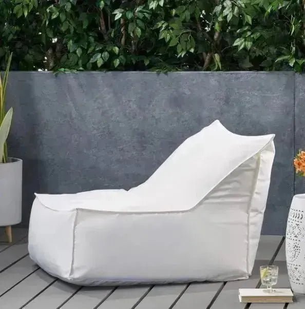 A soft, compact white COMFY FLOOR CHAIR by House of Effy is placed on a wooden deck with a gray concrete wall and greenery in the background.