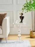 Load image into Gallery viewer, A House of Effy CLEAR ACRYLIC END TABLE with a dog bust sculpture and a white mug adds modern sophistication next to a white couch adorned with a brown pillow, complemented by a green potted plant in a woven basket, all set against a white paneled wall background.
