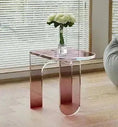 Load image into Gallery viewer, A small, transparent pink acrylic side table with a vase holding three white flowers on top, placed in front of a window with horizontal blinds. This ACYRLIC SIDE TABLE by House of Effy adds a touch of contemporary design to any room.
