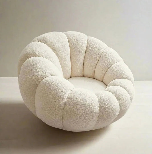 The House of Effy's PUMPKIN CHAIR, featuring a tufted design and plush cream color, sits snugly on a textured round rug in a child's room with beige walls.