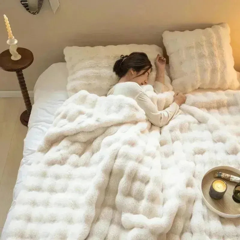 A person sleeps in a bed with a House of Effy TUSCAN THROW, enjoying winter warmth from the plush material. Next to them is a small round table with a lit candle and another candle in a holder on the wall.