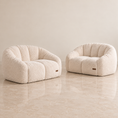 Load image into Gallery viewer, Two rounded boucle armchairs in a warm off-white/cream textured fabric, set on a polished beige marble floor against a matching beige wall.
