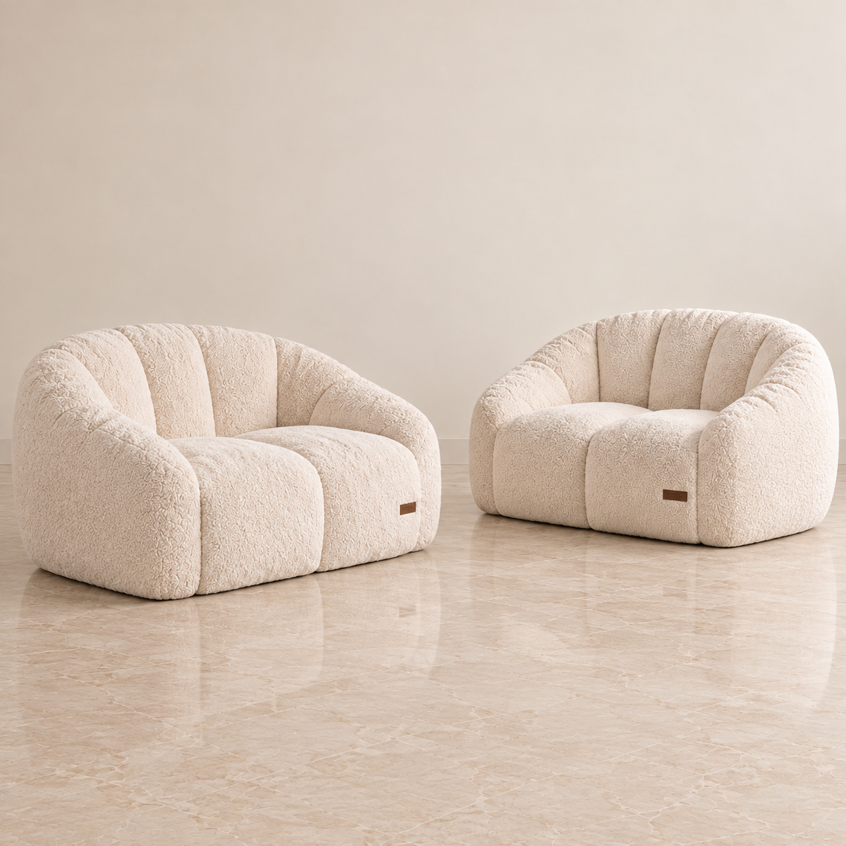Two rounded boucle armchairs in a warm off-white/cream textured fabric, set on a polished beige marble floor against a matching beige wall.