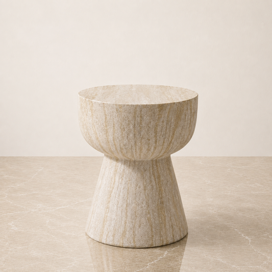 A modern pedestal stool made of textured beige travertine stone, set against a minimalist beige background.