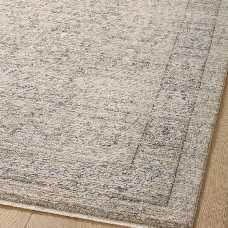 Amber taupe area rug close-up showing its distressed oriental pattern, textured surface, and decorative border on a light hardwood floor.