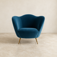 Load image into Gallery viewer, a barrel chair upholstered in deep teal velvet with tapered gold metal legs, set against a neutral beige textured wall and stone floor.

