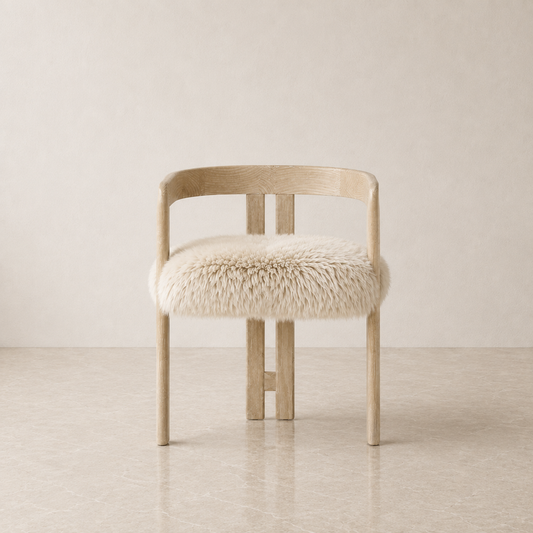 A light natural wood chair with a curved backrest and a fluffy cream sheepskin seat cushion, set against a minimalist beige wall and floor.