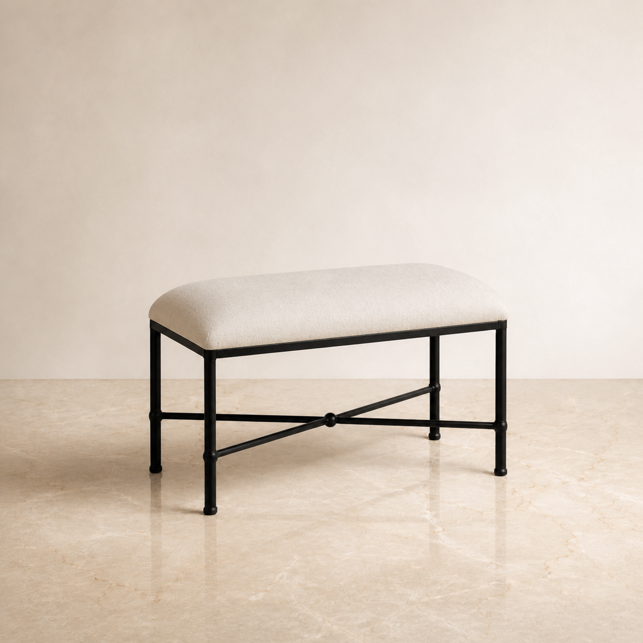 A rectangular upholstered bedroom bench with a cream fabric seat cushion and a black metal frame, set against a warm beige wall and light stone floor.