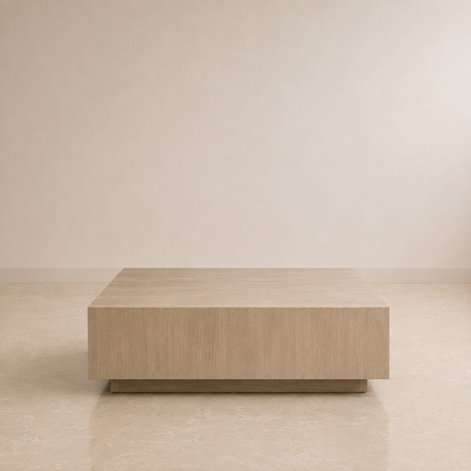 A low, rectangular coffee table with a light oak wood grain finish, positioned against a minimalist beige wall and tiled floor.
