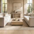 Load image into Gallery viewer, A modern living room setup featuring two off-white upholstered sofas facing a low wooden coffee table, set on a large beige rug in a bright, sunlit room with large windows and a console table in the background.
