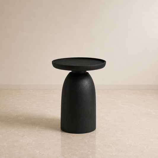A modern black ceramic side table with a wide circular tray top and a rounded pedestal base, set against a neutral beige background.