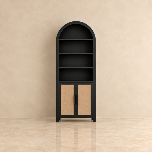 A tall black bookcase and cabinet with four open shelves on top and two cane-finish doors with gold handles on the bottom, set against a beige textured wall and floor.