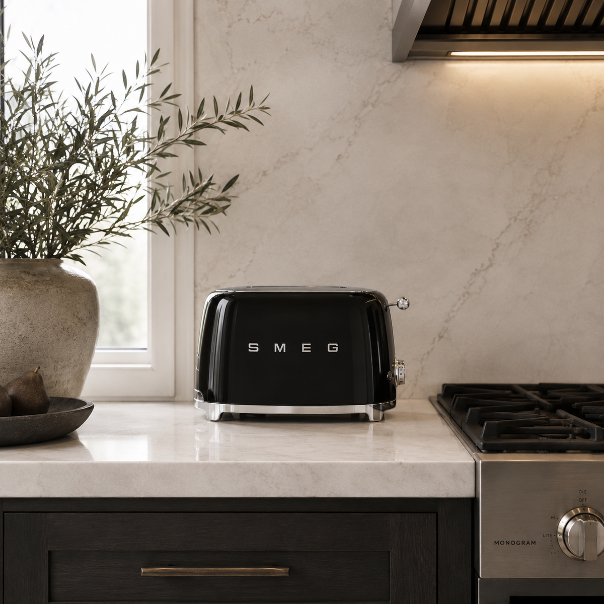 A black toaster sits on a white marble kitchen countertop, with a beige marble backsplash, dark wood cabinets, a gas stovetop, and a potted olive branch in the background.