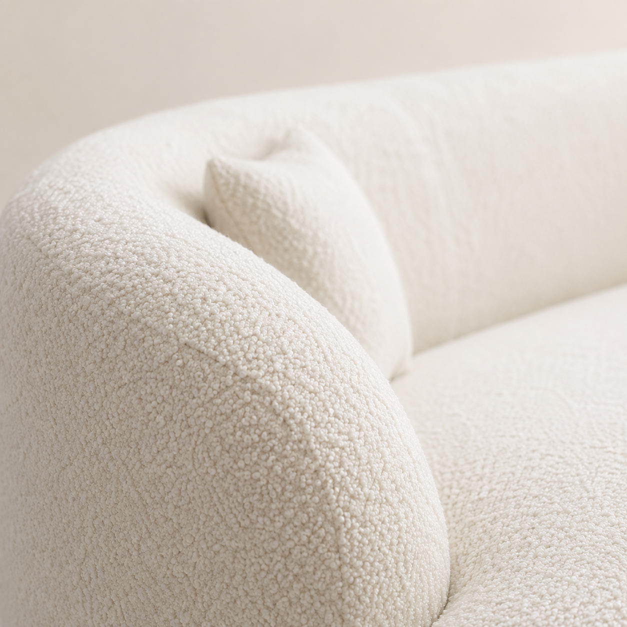 boucle curved sofa close-up of corner with a matching throw pillow, showing the soft textured fabric against a neutral light beige background.