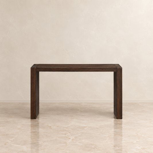 A dark brown wooden console table with a minimalist rectangular design, set against a neutral beige textured wall and marble floor.