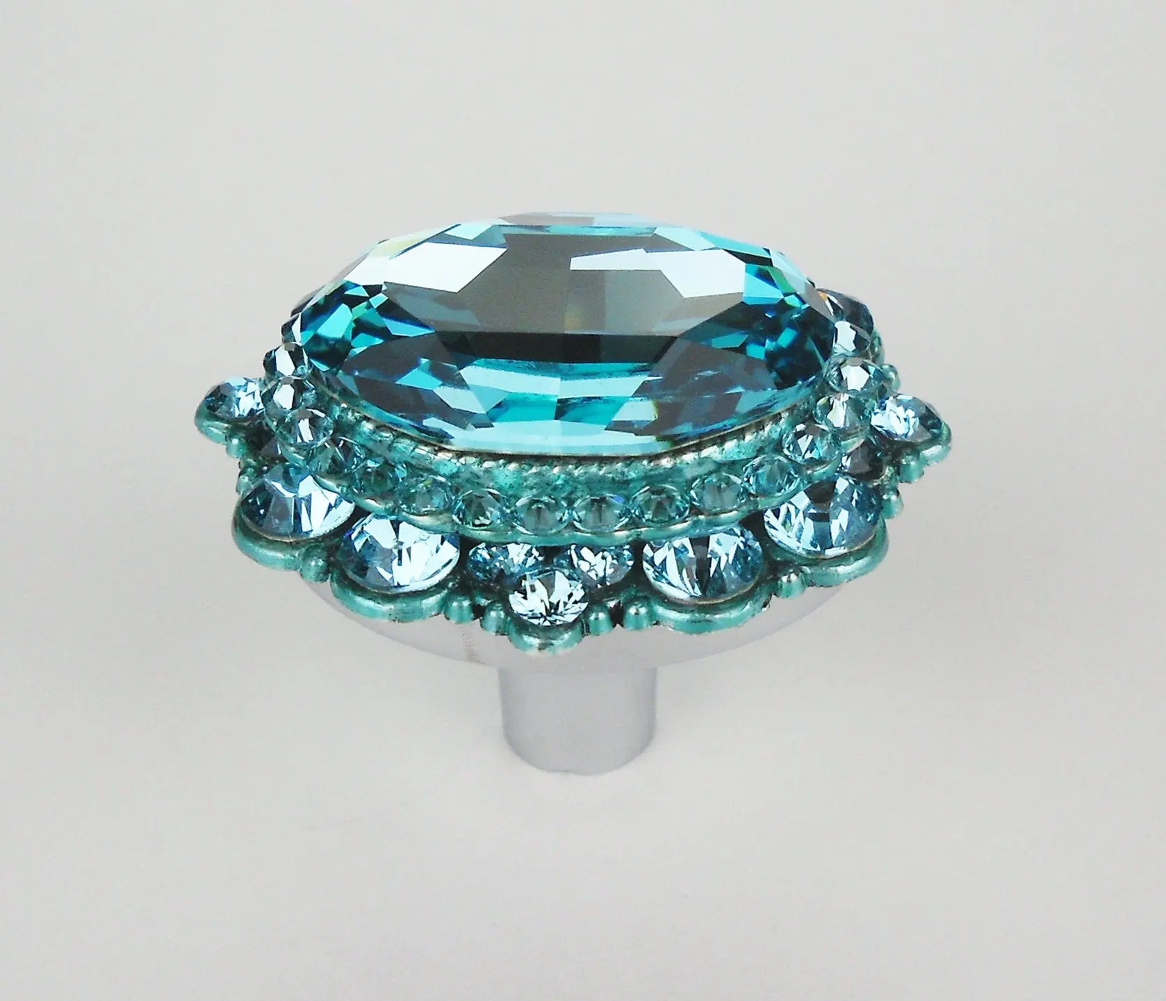 Elegant turquoise crystal cabinet knob with faceted oval center and round accents on polished silver base on white background