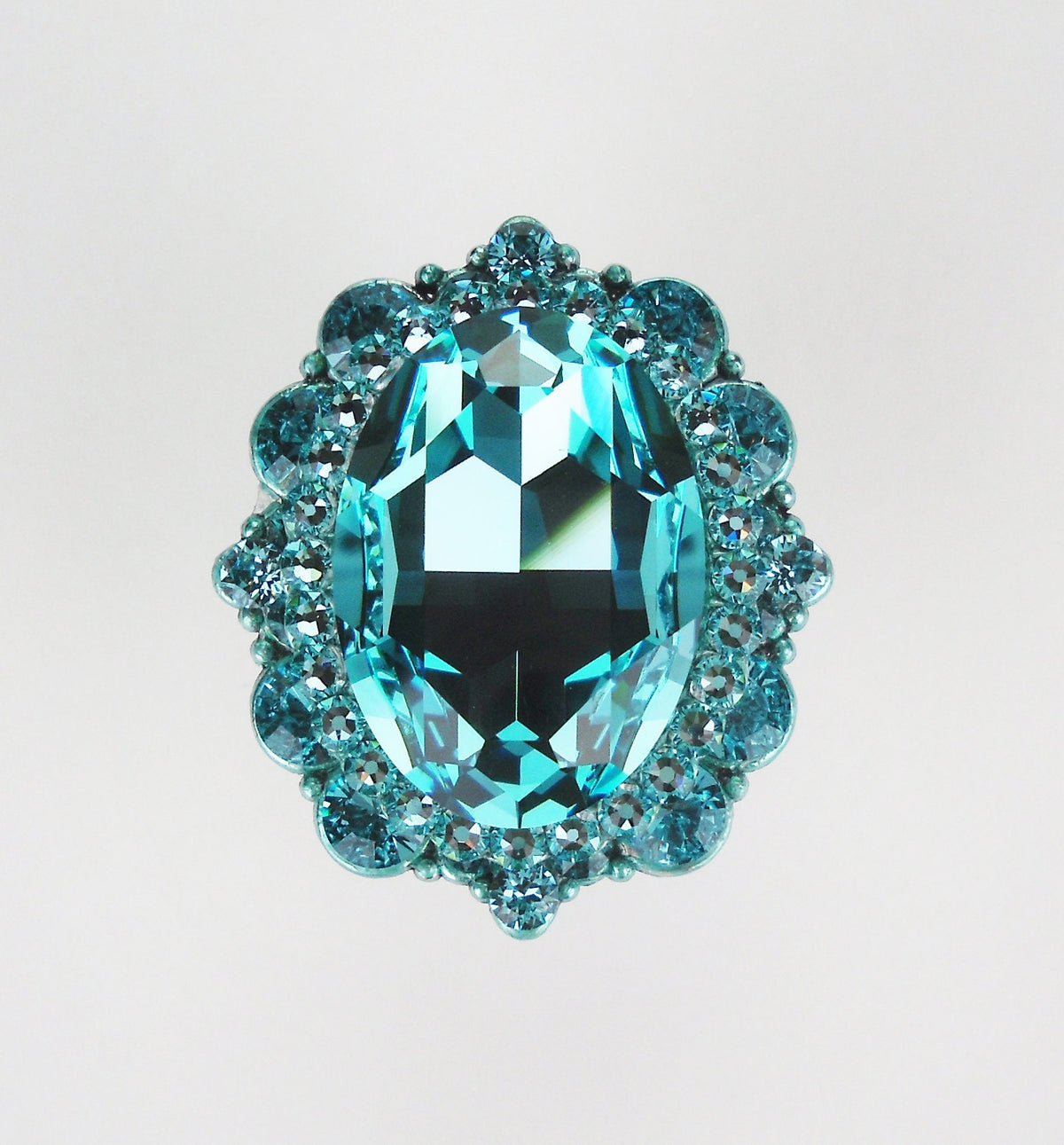 Close-up of an oval turquoise crystal cabinet knob with smaller round crystals in a polished silver setting on white background