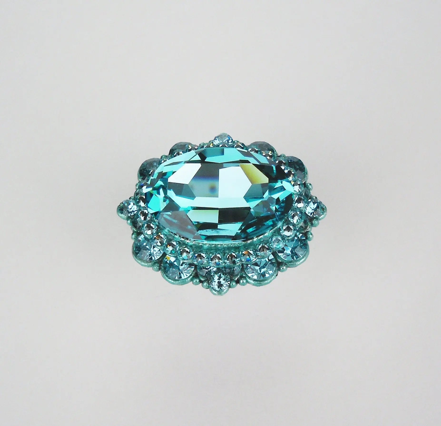 Elegant turquoise crystal cabinet knob with faceted oval center and smaller surrounding crystals on a neutral background