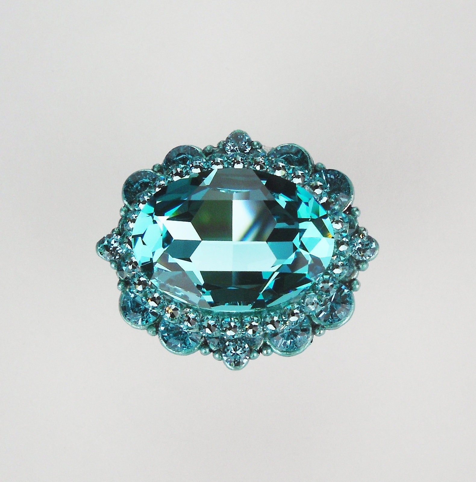 Oval turquoise crystal cabinet knob with intricate faceted detailing and polished metal base on white background