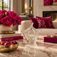 Load image into Gallery viewer, A crystal candy dish with a geometric diamond shape sits on a polished marble coffee table in a luxurious living room setting. The table is styled with a gold bowl of pink chocolates, a vase of vibrant pink peonies, and designer books, with a cream sofa and fireplace in the background.

