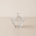 Load image into Gallery viewer, A clear glass lidded candy dish with a faceted geometric design, set on a light beige marble surface against a matching beige background.
