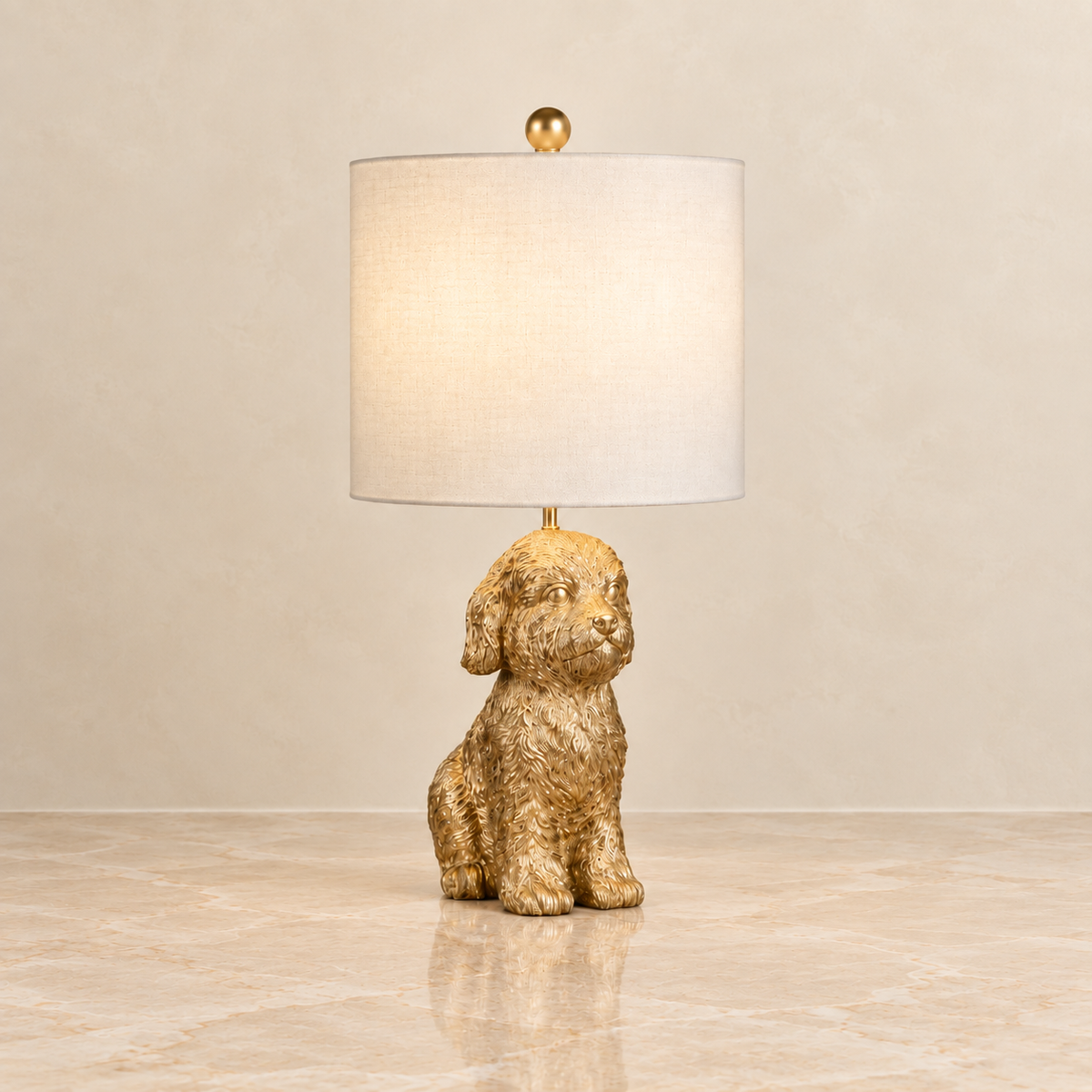 A table lamp with a textured gold dog-shaped base and a white fabric drum shade, shown on a polished marble surface against a neutral beige wall.