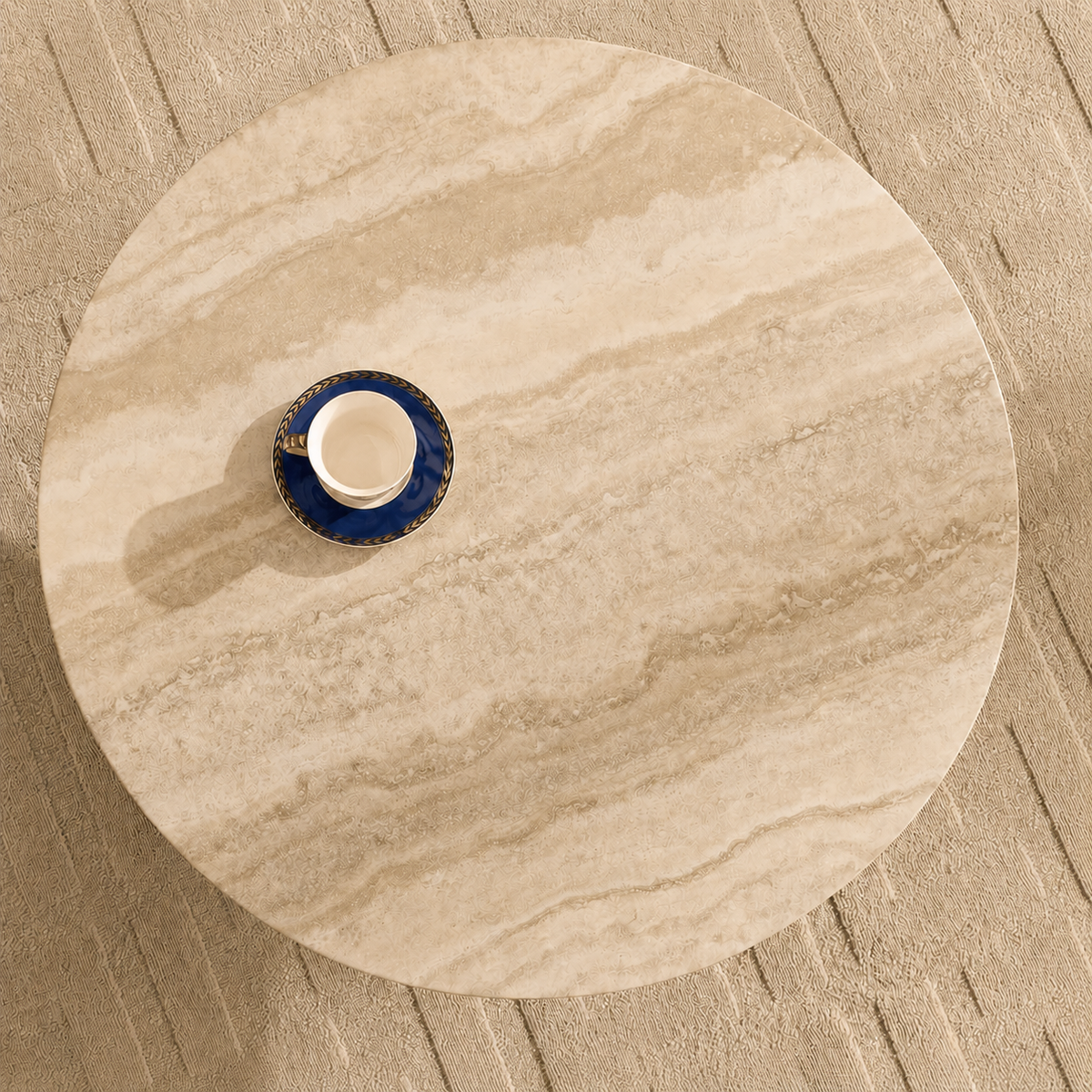 A round beige marble-patterned coffee table or tray with a small blue and white cup placed on top, photographed from above on a textured beige surface.