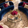 Load image into Gallery viewer, A luxury living room scene featuring two curved navy blue velvet sofas arranged in a circle around a glass-top coffee table. The room is styled with a textured beige and brown area rug, cream bouclé armchairs, and deep magenta and cream accent pillows.
