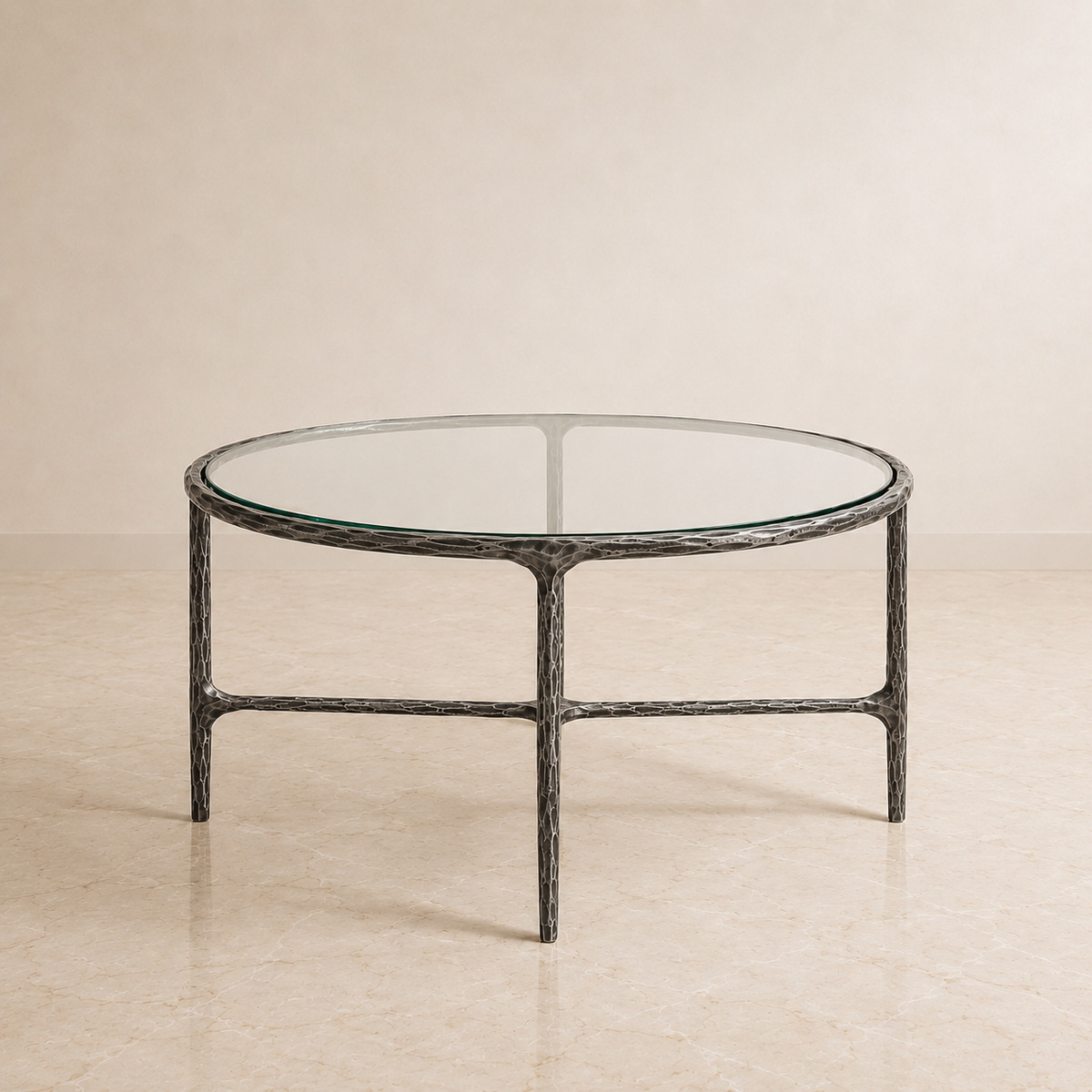 A round coffee table with a clear glass top and a textured dark gray metal frame, set against a neutral beige background.