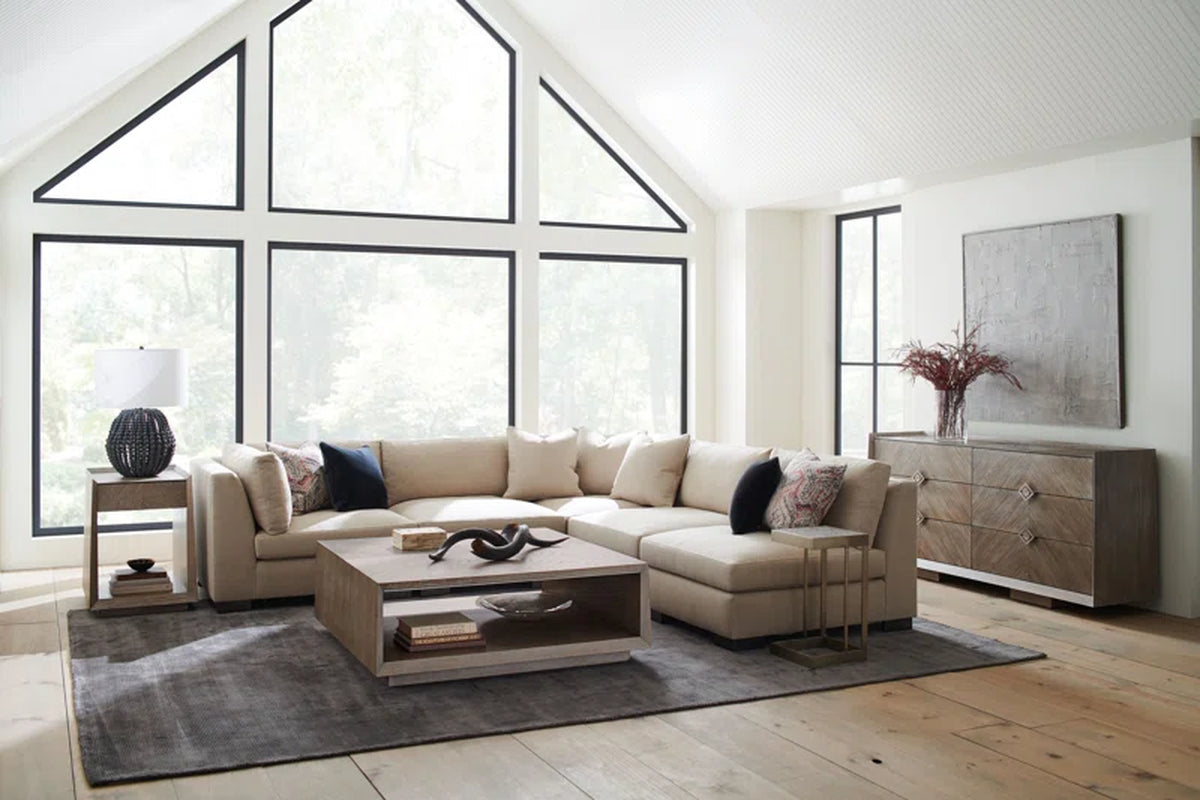 Contemporary living room with beige sectional sofa, geometric wooden coffee table, gray area rug, and large black-framed windows