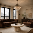 Load image into Gallery viewer, A luxury living room featuring a dark brown tufted sofa and matching armchair, a round marble coffee table, a large crystal chandelier, and a city view through tall windows.
