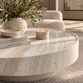 Load image into Gallery viewer, A round beige marble coffee table in a styled living room setting, decorated with a textured ceramic vase of olive branches, a small bowl, a lit candle, and stacked books.

