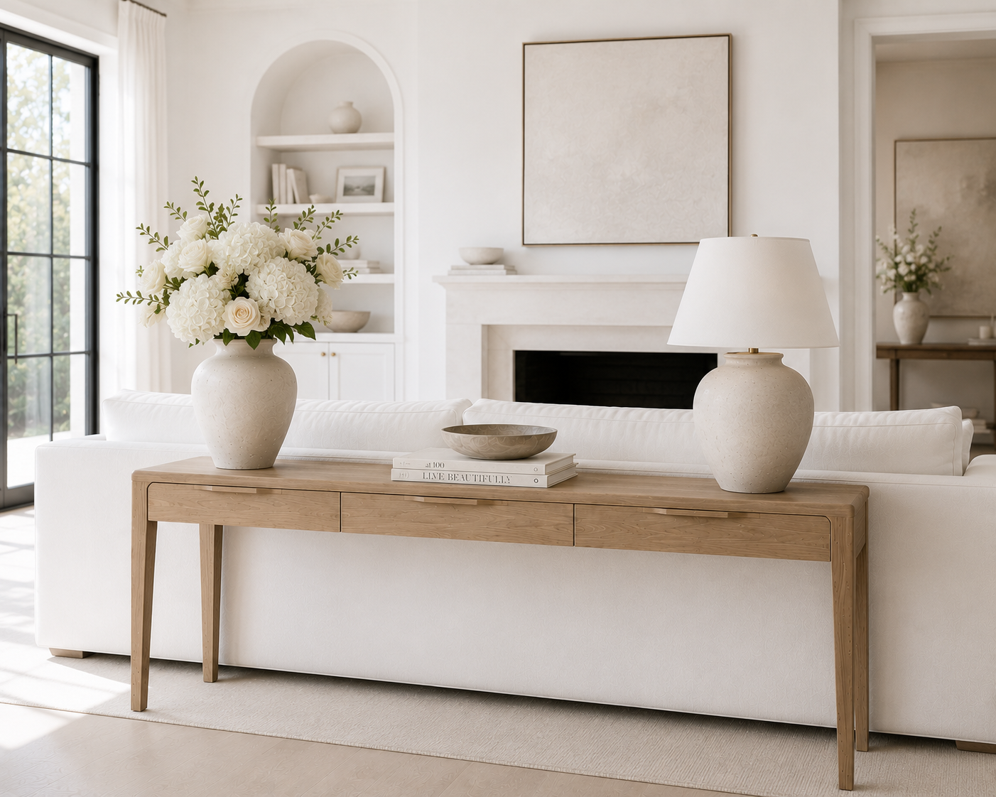 console table that is behind a sofa with flowers in a vase and a table lamp on it