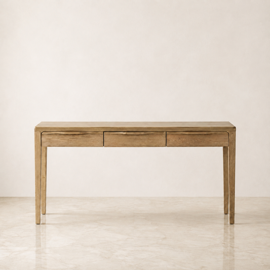A light natural wood console table with three drawers and slim legs, set against a minimalist beige wall and marble floor.