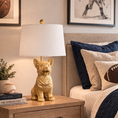 Load image into Gallery viewer, Gold Corgi Lamp with white drum shade on a wooden nightstand in a boy's bedroom with navy bedding and sports-themed decor.
