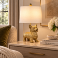 Load image into Gallery viewer, Gold Corgi Lamp with white drum shade on a marble side table beside a cream sofa with an olive green velvet pillow.

