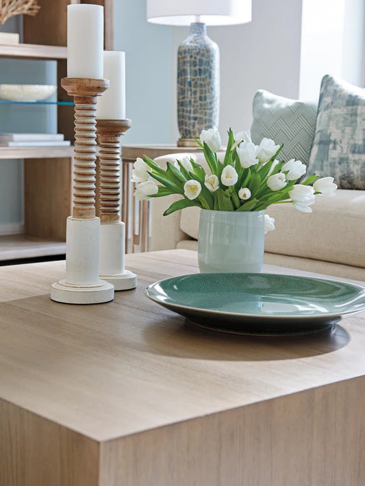 Square wooden coffee table with decorative candle holders, white tulips in vase, and green ceramic plate in living room