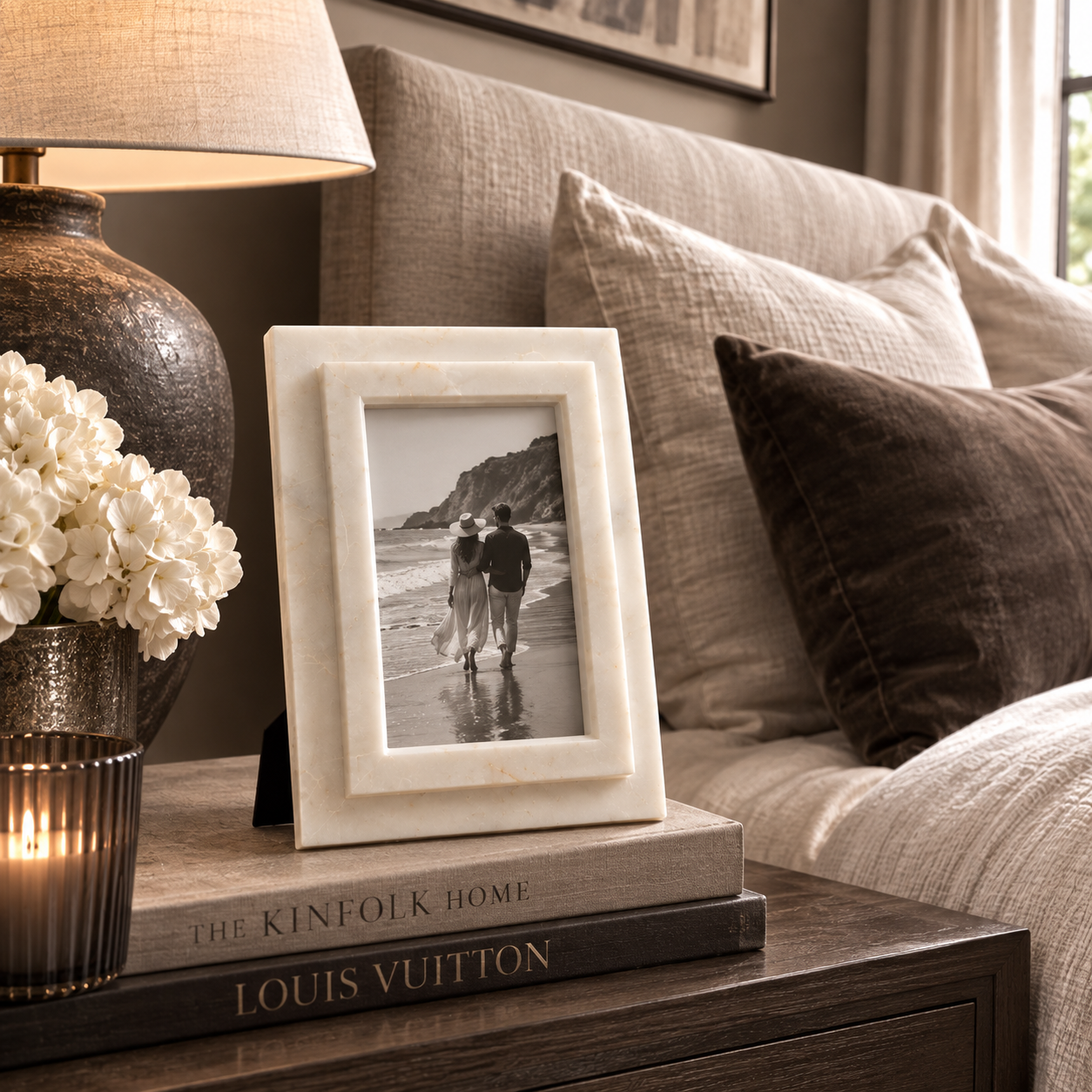 decorative frame holding a black-and-white beach photograph, styled on a wooden side table next to a lamp, flowers, and a Louis Vuitton book, with a sofa in the background.