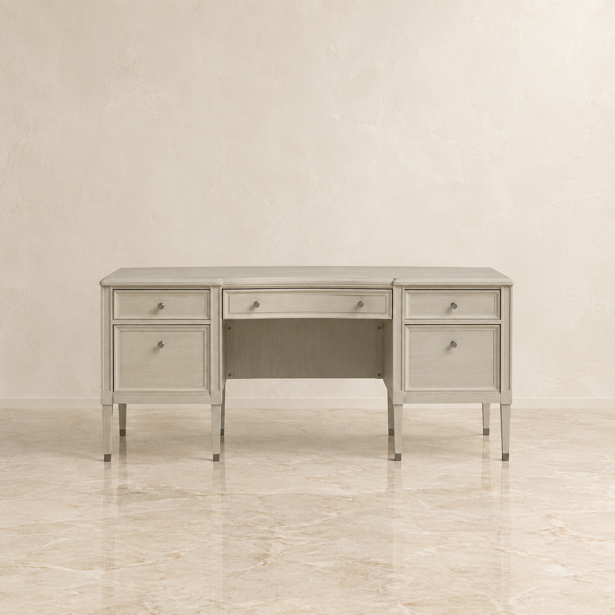 A light gray upholstered writing desk with three drawers, a center drawer, and an open center shelf, shown against a neutral beige textured wall and marble floor.