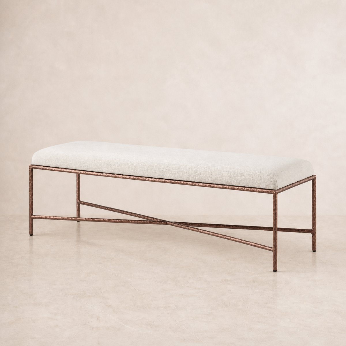 A modern fabric bench with a light beige upholstered cushion and a textured bronze metal frame, set against a neutral beige background.