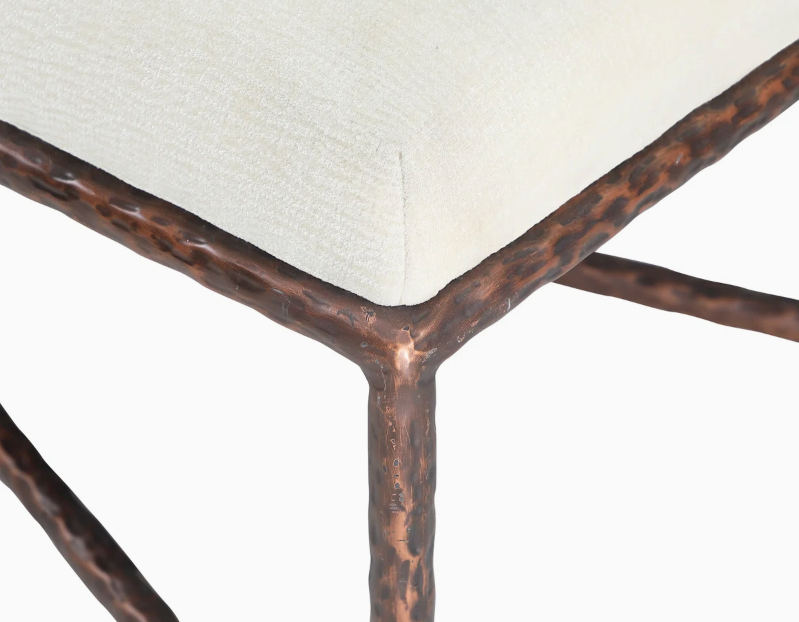 Close-up of beige chenille fabric seat cushion with textured hammered copper metal bench frame on white background