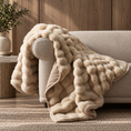 Load image into Gallery viewer, A chunky, textured faux-fur throw blanket in a warm cream/beige color, draped over the arm of a light beige sofa in a cozy, sunlit living room setting.
