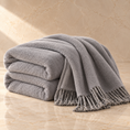 Load image into Gallery viewer, A stack of folded gray towels with fringed edges draped over a marble surface against a matching beige marble wall.

