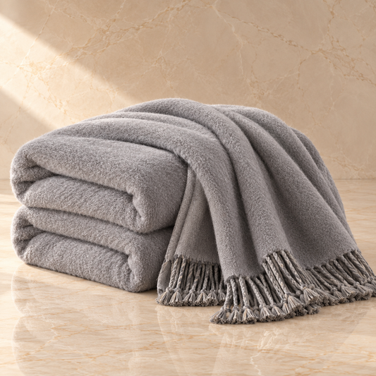 A stack of folded gray towels with fringed edges draped over a marble surface against a matching beige marble wall.